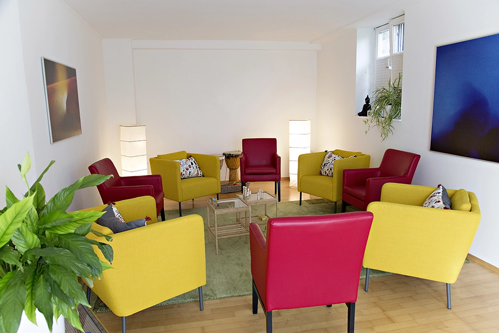 Heller Praxisraum mit roten und gelben Sesseln, gemütliche Gesprächsatmosphäre.