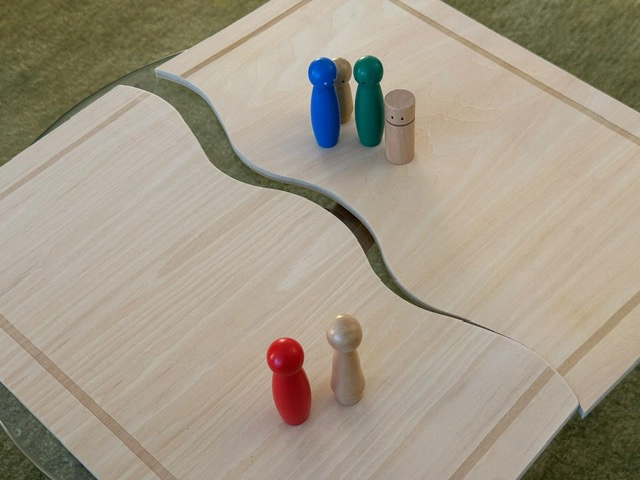 Holzbrett mit einer geschwungenen Form, auf dem sich bunte Spielfiguren befinden.